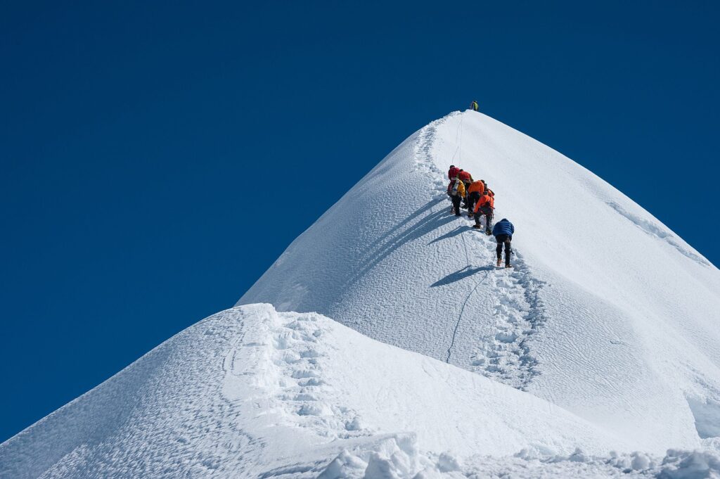 Grupo de pessoas escalando montanha coberta de neve, cenário que mostra a importância das melhores botas para neve em ambientes extremos.