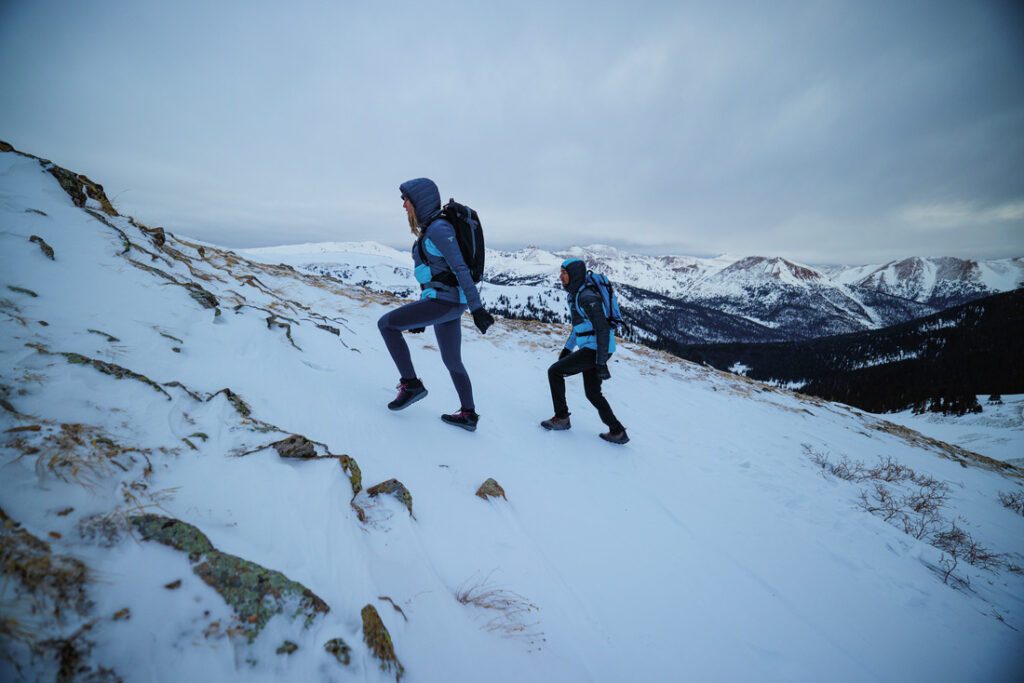 Casal caminhando em trilha de montanha coberta de neve, exemplo de quando usar as melhores botas para neve para garantir conforto e tração.