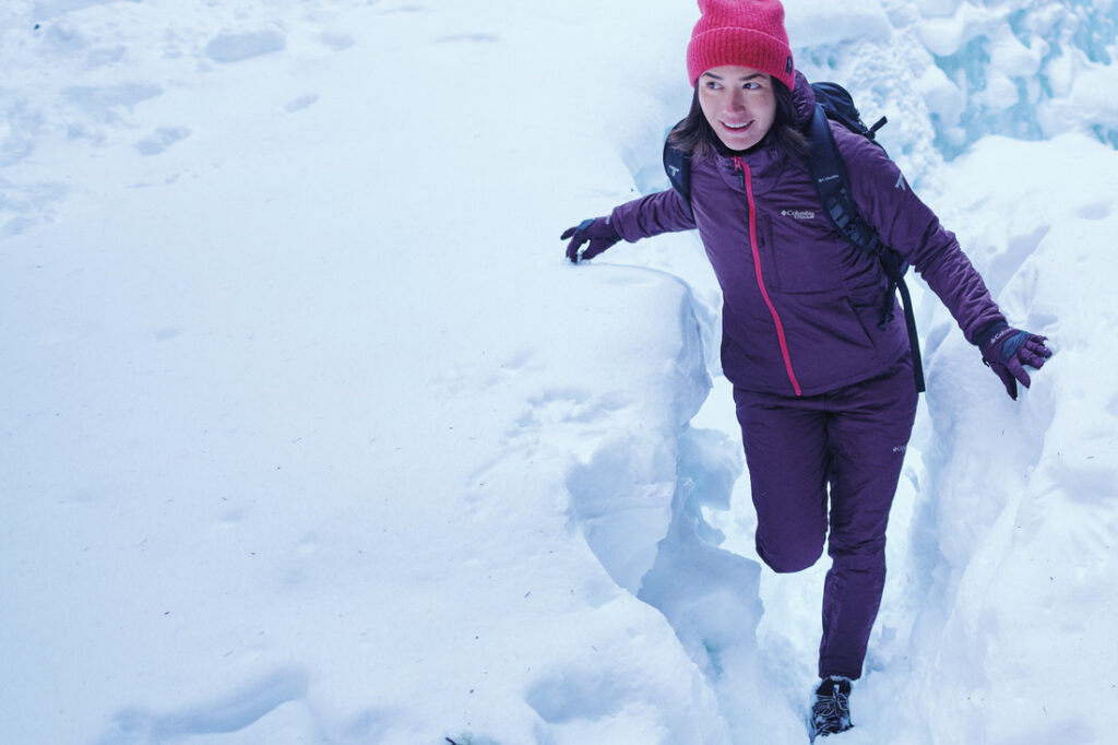Mulher caminhando em neve profunda com bota Columbia, ilustrando a diferença da melhor bota para neve feminina em relação a modelos comuns.