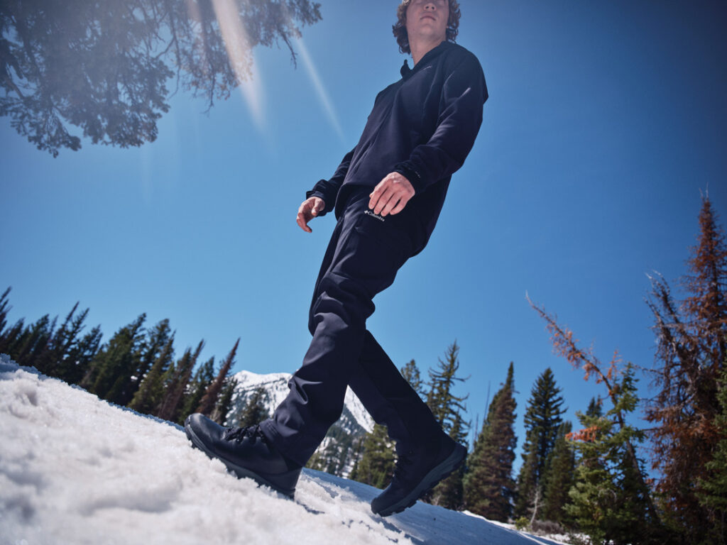 Homem com bota Columbia masculina caminhando em neve sob céu azul.