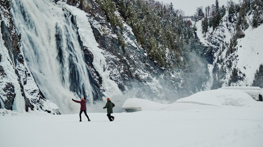 Casal caminhando em paisagem nevada com cachoeira ao fundo usando roupas de inverno Columbia.