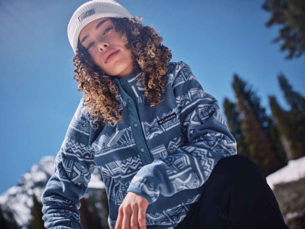 Pessoa usando fleece Columbia azul com padrão geométrico em ambiente de neve, ilustrando a camada intermediária do sistema térmico de roupas para frio.