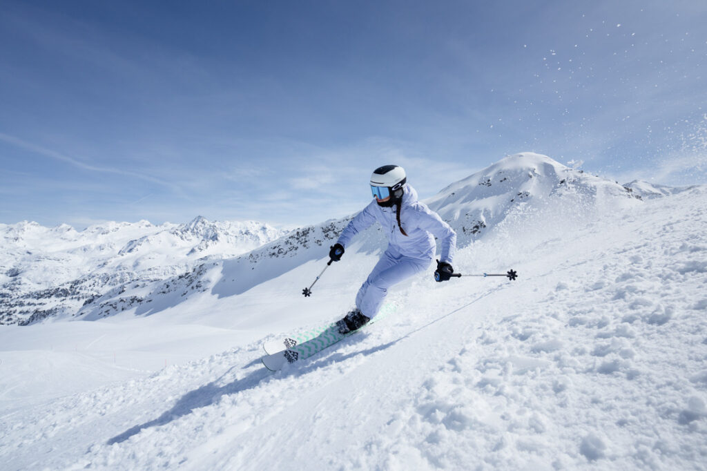 Pessoa esquiando com roupa Columbia branca em montanha nevada, representando o conjunto completo de roupas de ski.