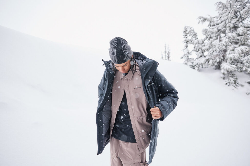 Pessoa vestindo jaqueta e roupa térmica Columbia em ambiente de neve, demonstrando o sistema de camadas para isolamento e conforto térmico.