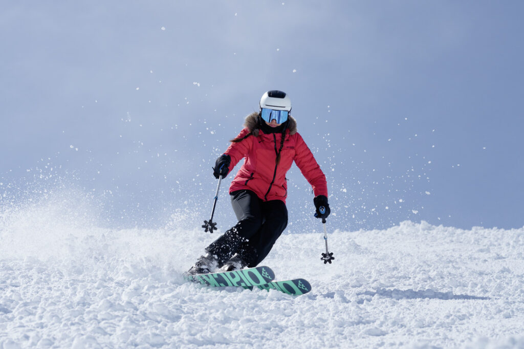 Pessoa esquiando com jaqueta Columbia vermelha em neve profunda, demonstrando aquecimento e proteção.